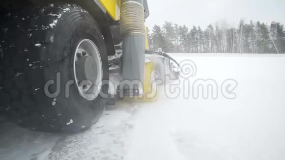 摄像机跟随重型车轮机械用巨大的旋转刷子在雪地里清除道路上的积雪视频的预览图