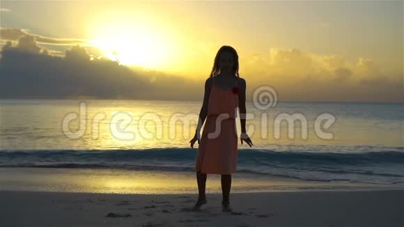 日落时在白色海滩上可爱的活泼的小女孩的剪影流动人口视频的预览图