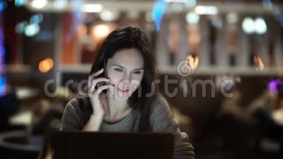 年轻漂亮的女人坐在咖啡馆里打电话布鲁内特女士晚上在笔记本电脑上工作视频的预览图
