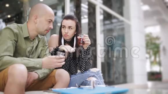 男人和女人在街头咖啡馆喝茶看智能手机上的照片视频的预览图