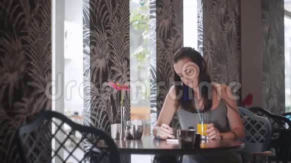年轻的女学生用智能手机发短信在咖啡馆喝橙汁视频的预览图
