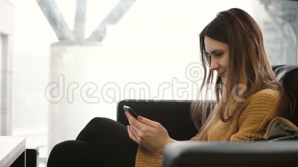 年轻的黑发女人坐在靠近窗户的咖啡馆里用智能手机有魅力的女性在网上聊天视频的预览图