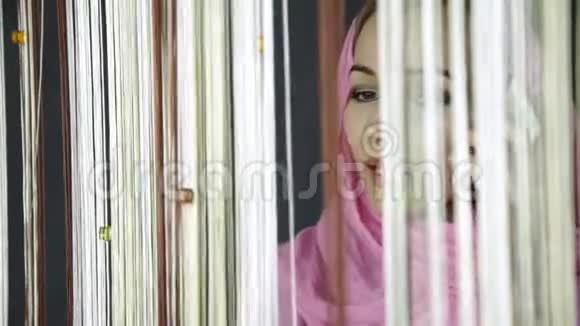 年轻的阿拉伯穆斯林妇女身穿粉红色头巾望着窗外向朋友挥手视频的预览图