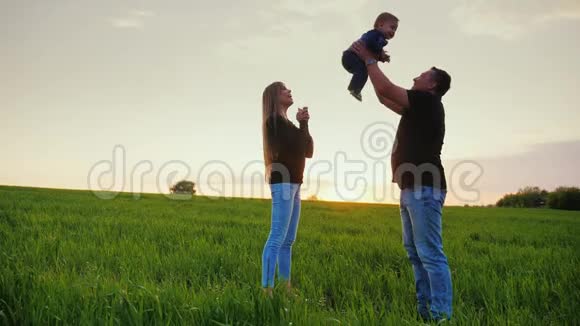 快乐的父母和一岁的儿子玩一个健康的父亲把儿子扔上去妈妈站在他旁边幸福的家庭视频的预览图