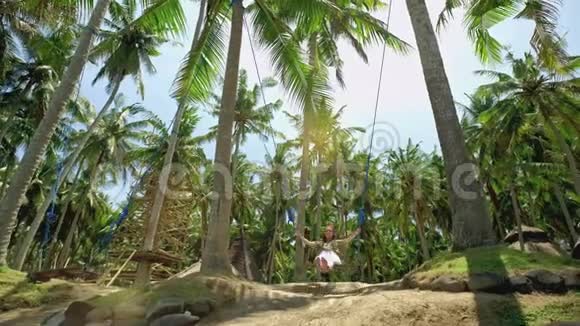 一个女孩在秋千上荡秋千看着热带海滨的日落自由休息度假旅行概念视频的预览图