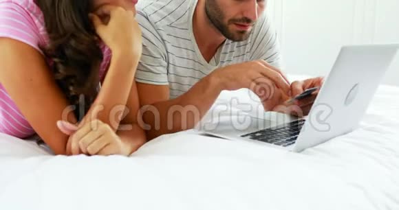 一对夫妇在卧室里用笔记本电脑上网购物视频的预览图
