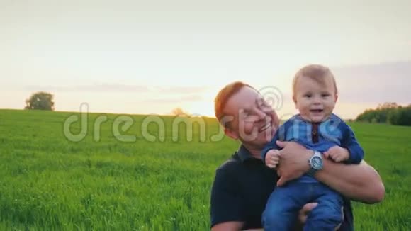 一个年轻快乐的父亲把一年的儿子抱在怀里在日落时风景如画的地方慢速视频视频的预览图