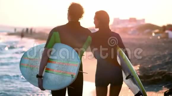一对年轻的男女冲浪者穿着湿衣服在海滩上散步手里拿着冲浪板你看视频的预览图