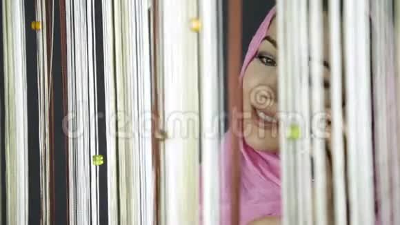 年轻的阿拉伯穆斯林妇女身穿粉红色头巾望着窗外向朋友挥手视频的预览图