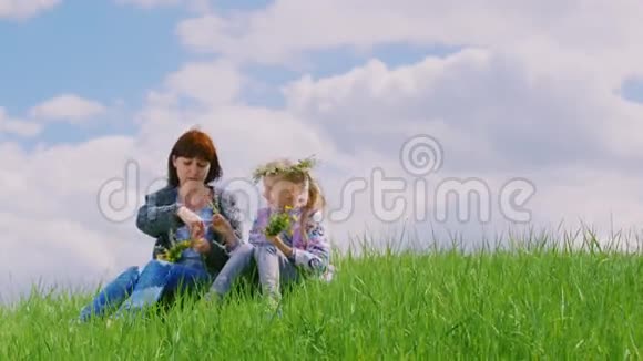 一个年轻的女人和她的女儿一起花圈坐在风景名胜区的草地上靠着一片绿草视频的预览图