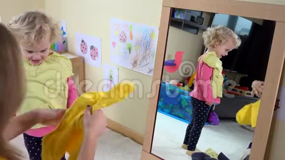可爱的女孩妈妈在派对前通过镜子挑选衣服视频的预览图