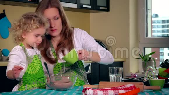 女人把油倒在蛋糕面团里小帮手女儿用勺子搅拌视频的预览图