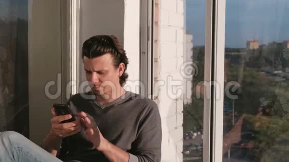 男人看着手机在夕阳下坐在阳台上的社交网络里翻着带子视频的预览图