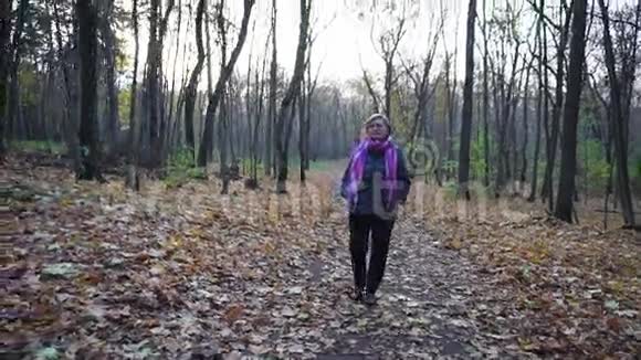 在秋天的树林里走着一位留着短发戴着眼镜的老妇人视频的预览图