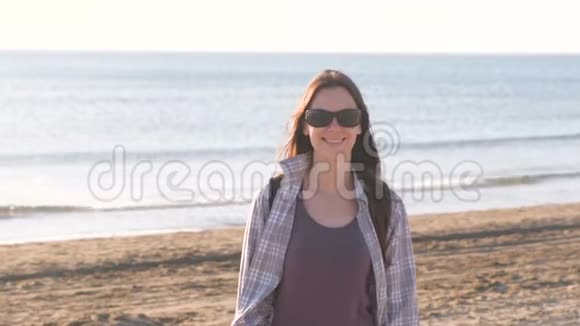 在海边的沙滩上戴着太阳镜的快乐年轻微笑的黑发女人视频的预览图