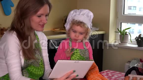 可爱的妈妈教女儿做饭家庭女孩看平板电脑视频的预览图