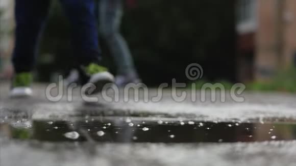 低角度特写无法辨认的孩子在雨后的夏天穿过水坑在水坑里奔跑的无忧无虑的孩子视频的预览图