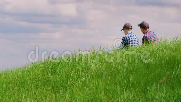 两个年轻人坐在青山上交流和梦想在美丽的蓝天背景下视频的预览图