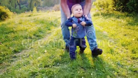 有趣的小男孩学会走路他的手由他父亲支撑男孩笑了手里拿着一朵丁香花视频的预览图