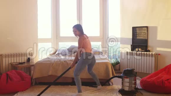 漂亮的女人正在家里用现代吸尘器在地板上盘旋听音乐和跳舞家务活视频的预览图