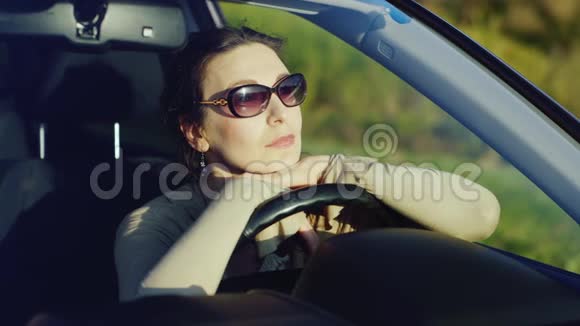 一个戴太阳镜的女人在车里放松坐在车轮后面欣赏日落时的美景快乐的司机视频的预览图