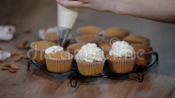 女性手拿着装满奶油奶酪和咖啡霜装饰纸杯蛋糕的管道袋视频的预览图