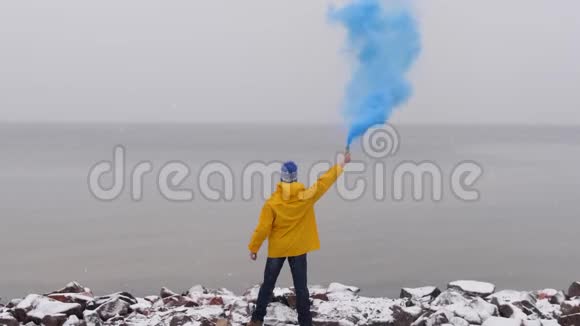 蓝色烟雾的人的后景穿着黄色外套在冰冻的大海前前景下的雪视频的预览图