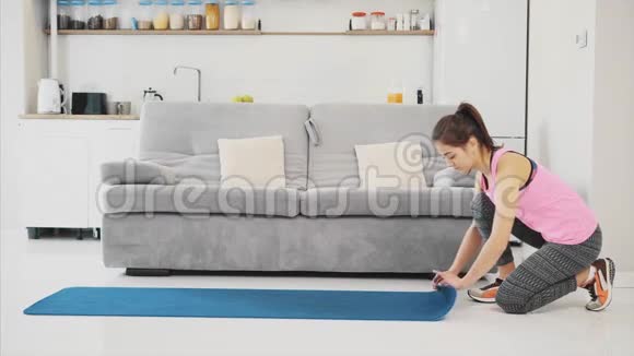 一位年轻漂亮的女士穿着蓝色慢跑或健身垫在家工作后在客厅里关门视频的预览图