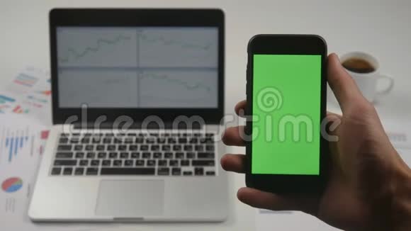 人使用智能手机绿色屏幕色度键在白色办公桌上笔记本电脑在后台上景男性视频的预览图