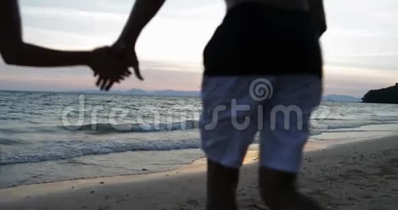 情侣在海上奔跑双手背对后景日落时分欢乐的男人和女人在海滩上视频的预览图