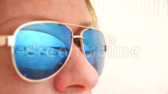 一个戴太阳镜的快乐女人的特写脸与休息的人的海滩反映在眼镜上4k慢视频的预览图