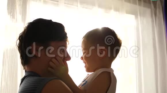 年轻的父亲抱着他的孩子靠近窗户阳光透过窗户孩子的欢笑和喜悦视频的预览图