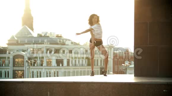 一位留着卷发的年轻女子穿着小短裤表演迷人的舞蹈日落视频的预览图