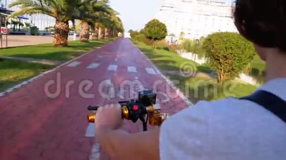 在度假小镇上一个骑着棕榈树的红色自行车道上骑着电动滑板车的女人视频的预览图
