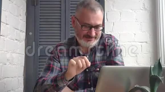 一位留着胡须的男会计师在一台笔记本电脑后面的家里工作在极简主义的室内环境背景下做了一份报告视频的预览图