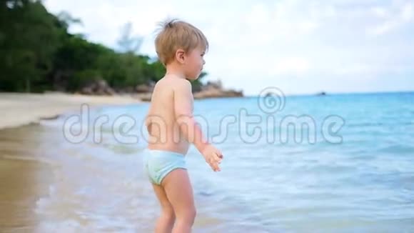 一个孩子沿着海滨快乐地散步3这个孩子正站在晴天的海浪中视频的预览图