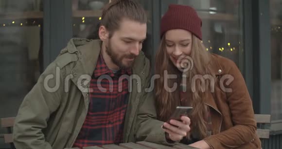 漂亮的夫妇坐在户外餐馆里看智能手机视频的预览图
