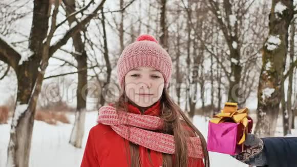 冬天一个美丽的年轻女学生站在一片白雪皑皑的森林里从朋友手中得到一份快乐的礼物视频的预览图