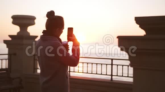 年轻女士在日出时在智能手机上慢镜头拍摄大海视频的预览图