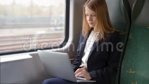 年轻商务女性坐火车在笔记本电脑上工作看着窗户视频的预览图
