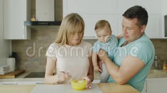 一位年轻的母亲准备吃她10个月大的儿子父亲站在他旁边把孩子抱在怀里宝贝视频的预览图