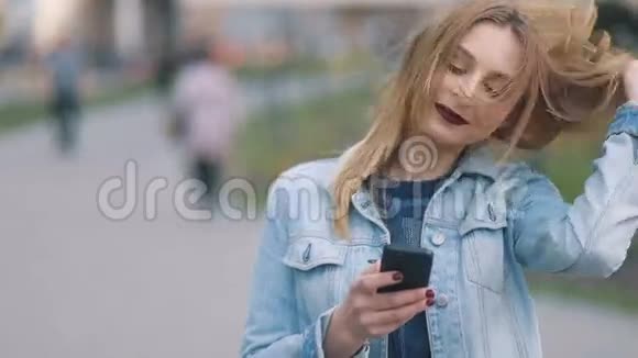 美丽迷人的年轻快乐金发女孩在布莱德尼姆法庭严格的模糊和深红色的嘴唇使用她的智能手机视频的预览图