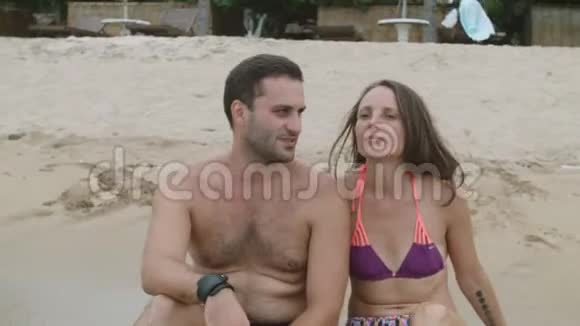 幸福的一家人坐在被海浪冲刷的沙滩上视频的预览图
