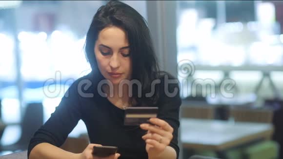 穿着时髦黑色连衣裙的漂亮白种人深色头发试图在办公室背景下用智能手机付款视频的预览图