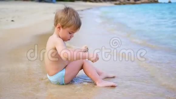 孩子正坐在沙滩上在阳光明媚的日子里在海浪中游泳视频的预览图