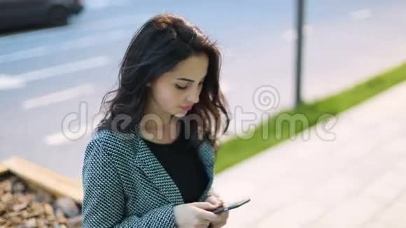 穿着严格的灰色夹克和黑色连衣裙深棕色头发的年轻温柔的商务女孩住在城市街道上视频的预览图
