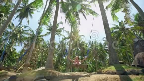 一个女孩在秋千上荡秋千看着热带海滨的日落自由休息度假旅行概念视频的预览图