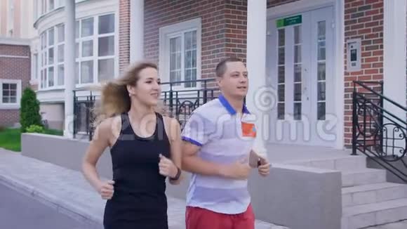 一个有魅力的女人和她成年的丈夫从事体育运动年轻的配偶沿着城市建筑奔跑他们喜欢一个人视频的预览图