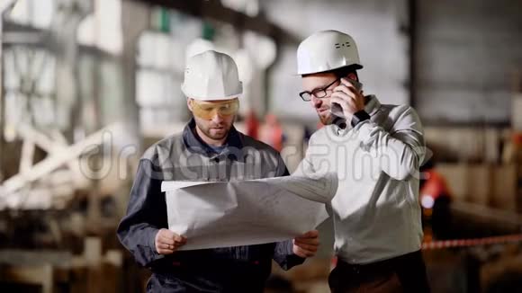 两名男工程师站在建筑现场并持有施工计划在电话里说话的设计师视频的预览图