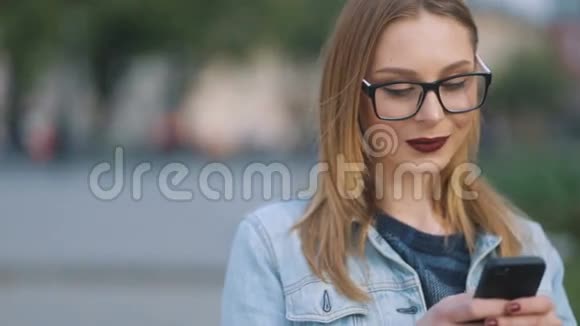 在街上用手机拍摄的戴眼镜的年轻时髦美女的肖像Stedicam慢镜头视频的预览图